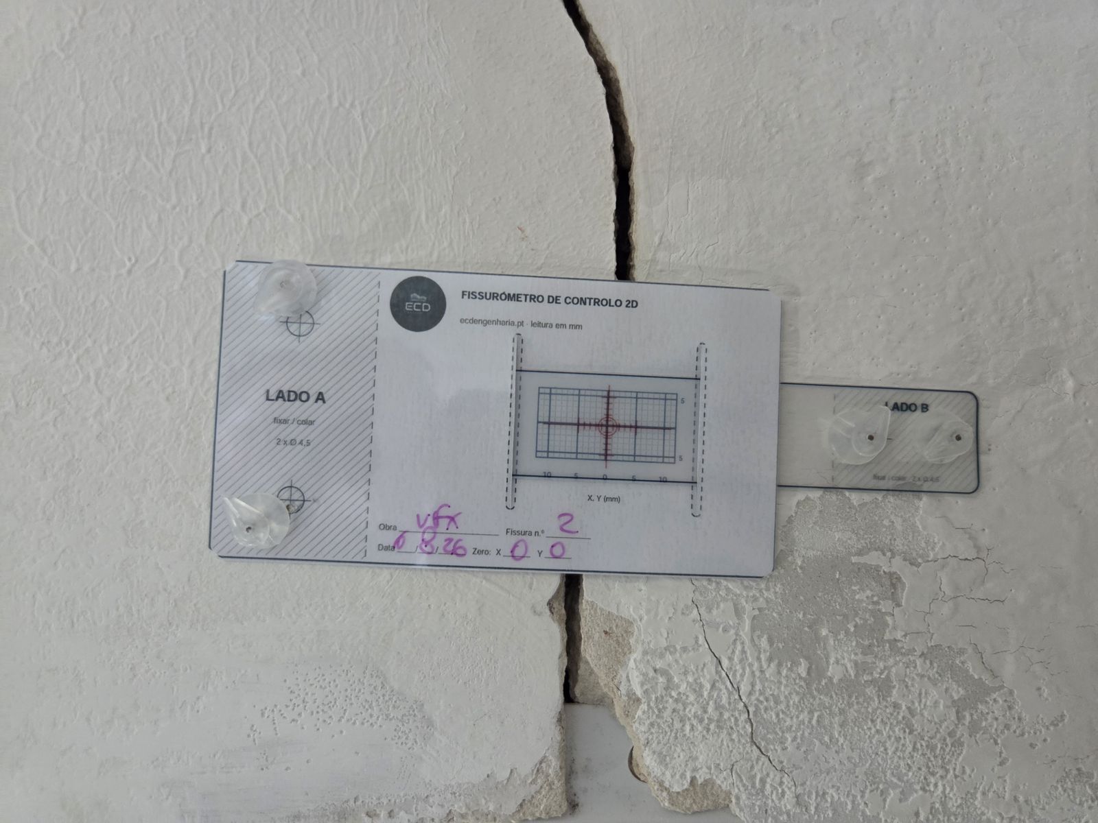 Fissurómetro de controlo 2D ECD instalado sobre fissura ativa em parede exterior, com registo de obra, número de fissura e leitura zero
